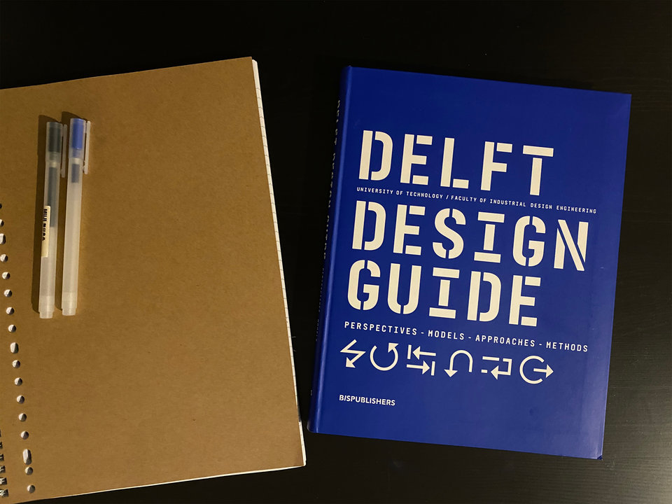 The print edition of the Delft Design Guide on a table with a notebook and pens.
