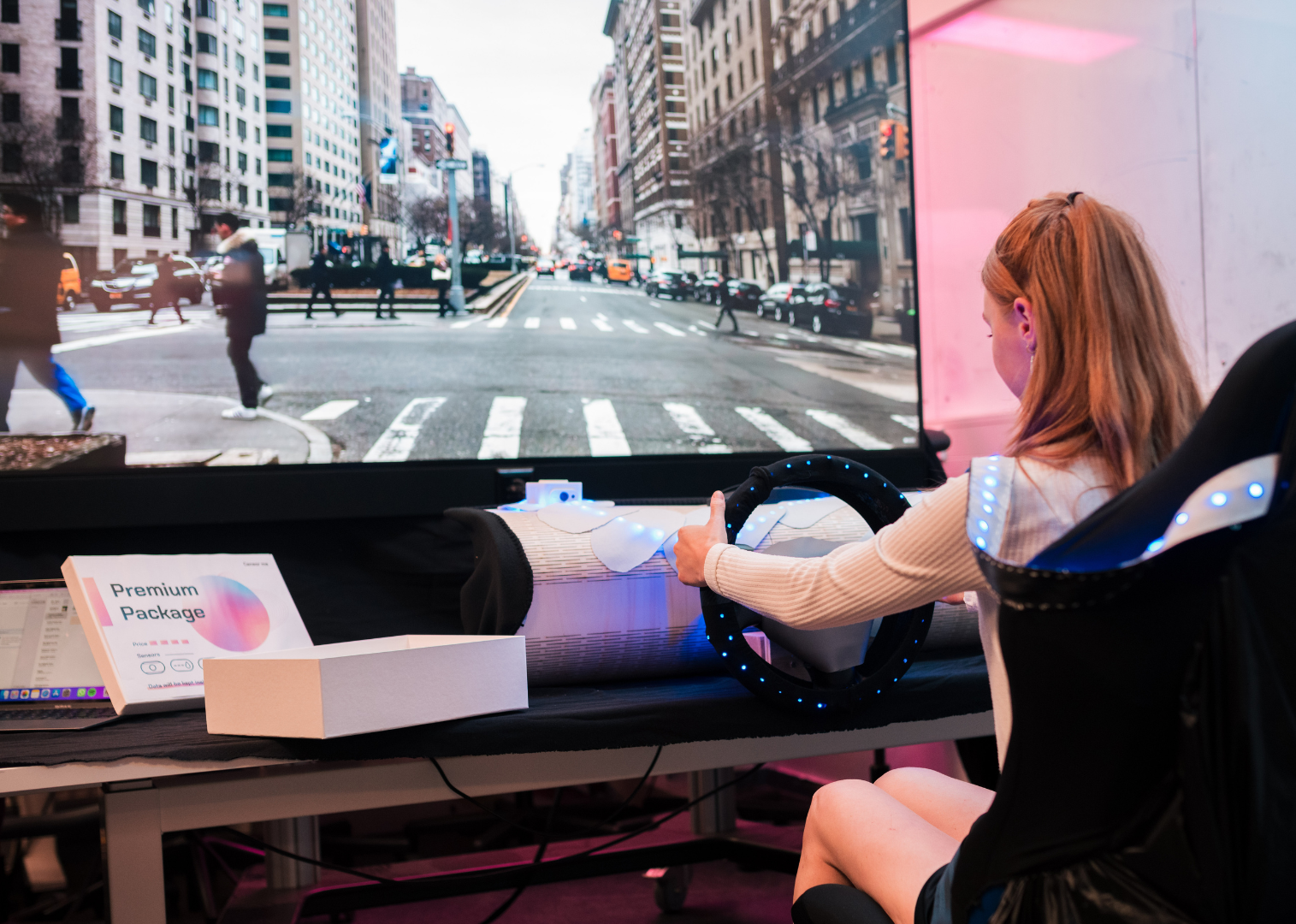 Woman testing the driving simulator in front of a big screen with a real life street view displayed on it.